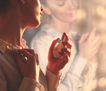 Stylish woman in blouse spraying a bottle of favorite perfume at sunset