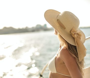 A woman stands in a yacht, wearing a white sun hat and an off-white bra top.