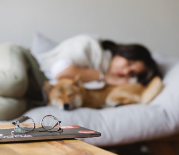 A lady with her pet dog lying on a couch